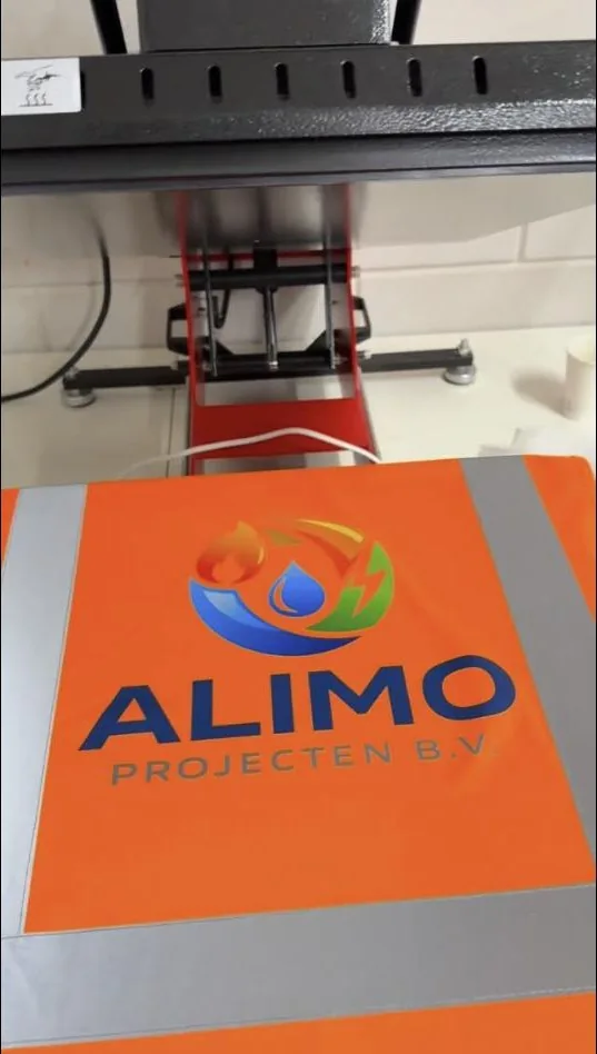 Logo van Alimo Projecten wordt op een oranje shirt geperst